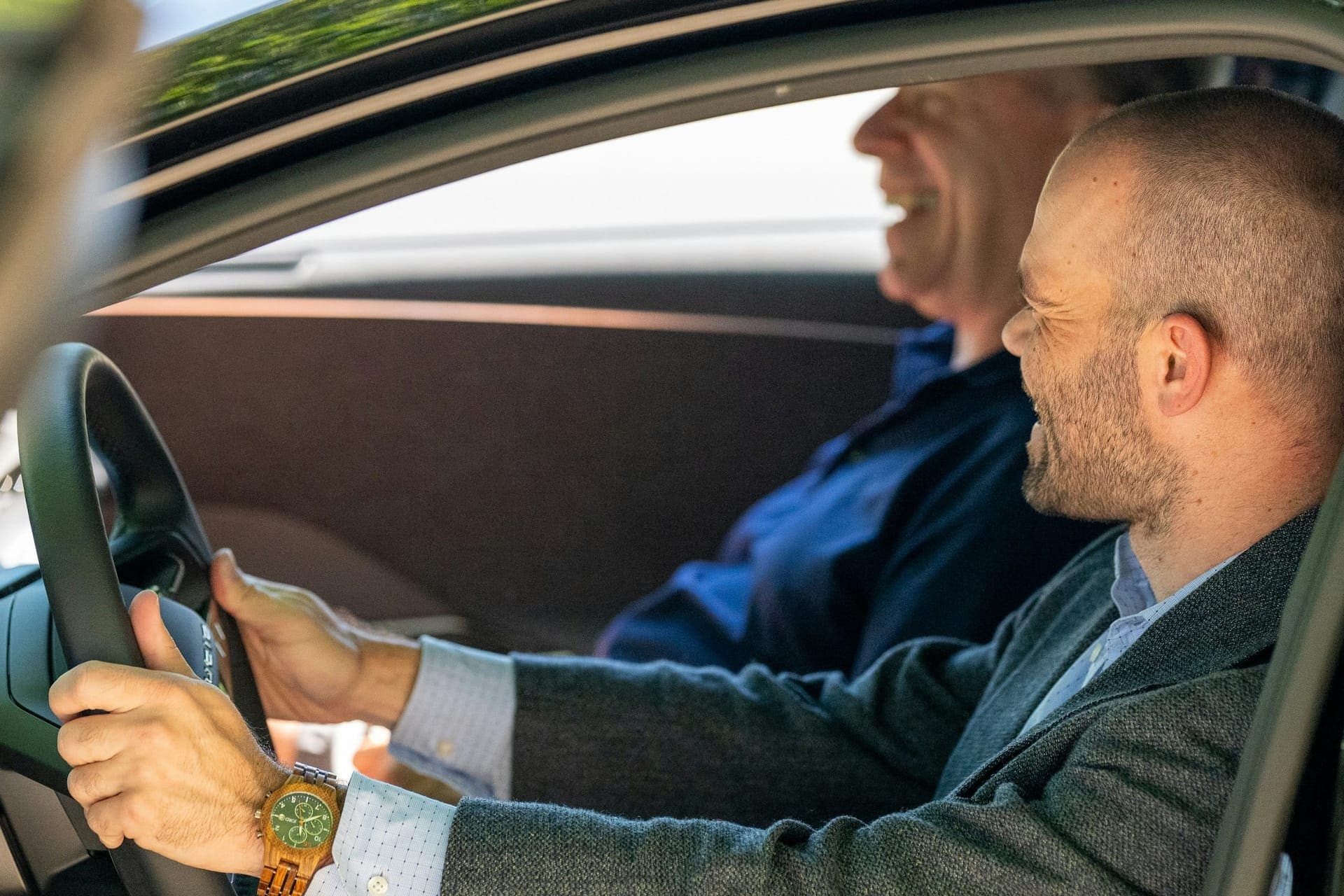 Zwei Menschen im Auto im goldenen Abendlicht, entspannt und lachend am Steuer
